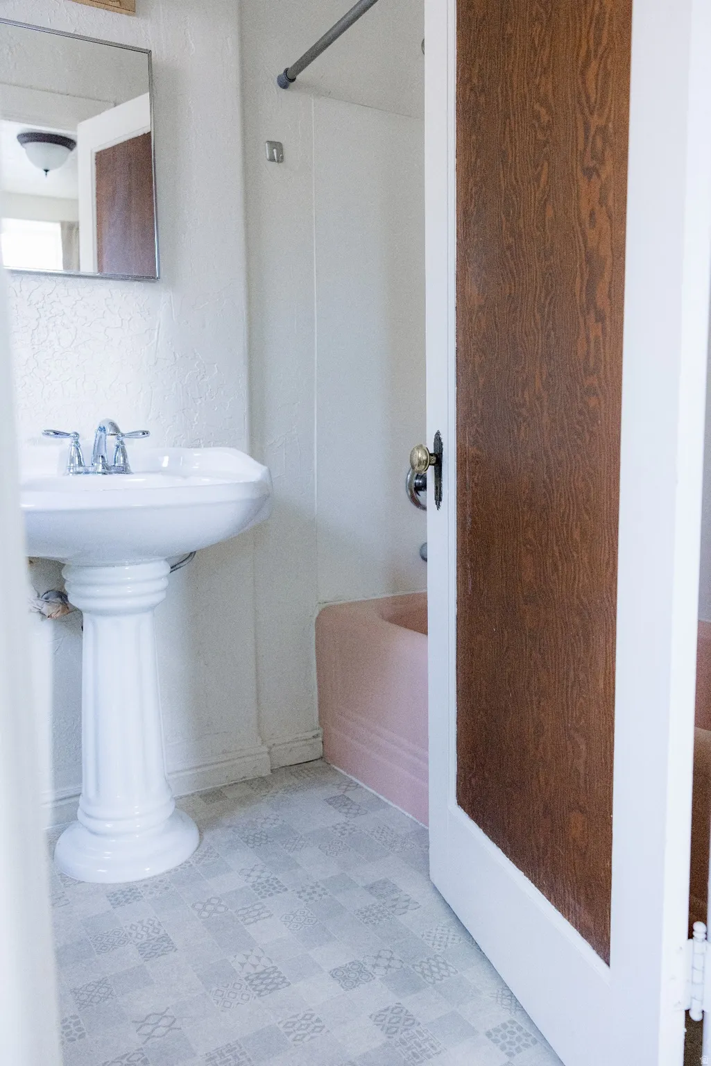 Bathroom featuring a pedestal sink, chrome faucet, wall-mounted mirror, and patterned floor tiles