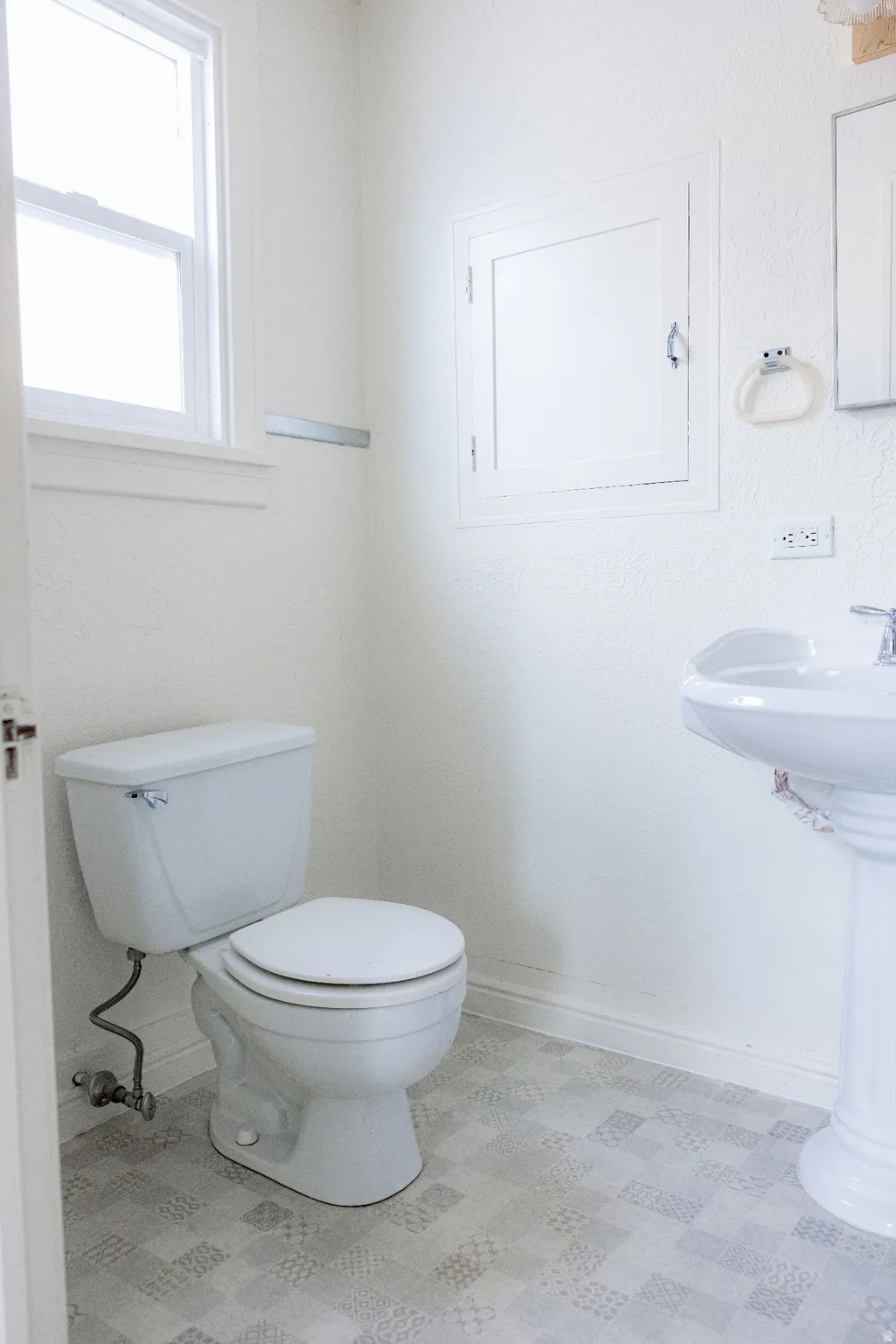 Bathroom with a pedestal sink, white toilet, and patterned tile-look flooring