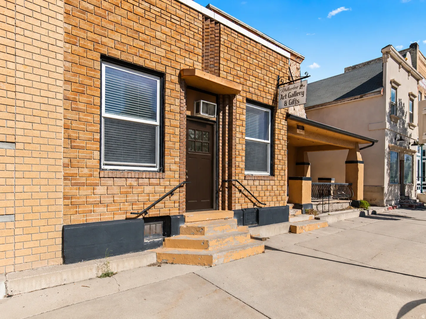 Brick exterior with a covered entryway, multiple windows, and a black handrail