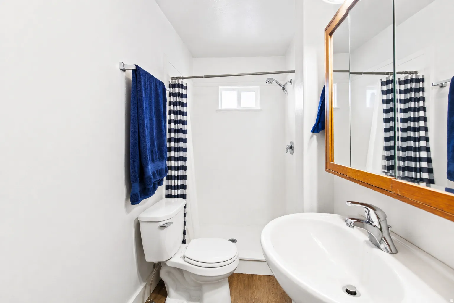Bathroom with a wall-mounted sink, a wood-framed medicine cabinet, and a shower with a small window