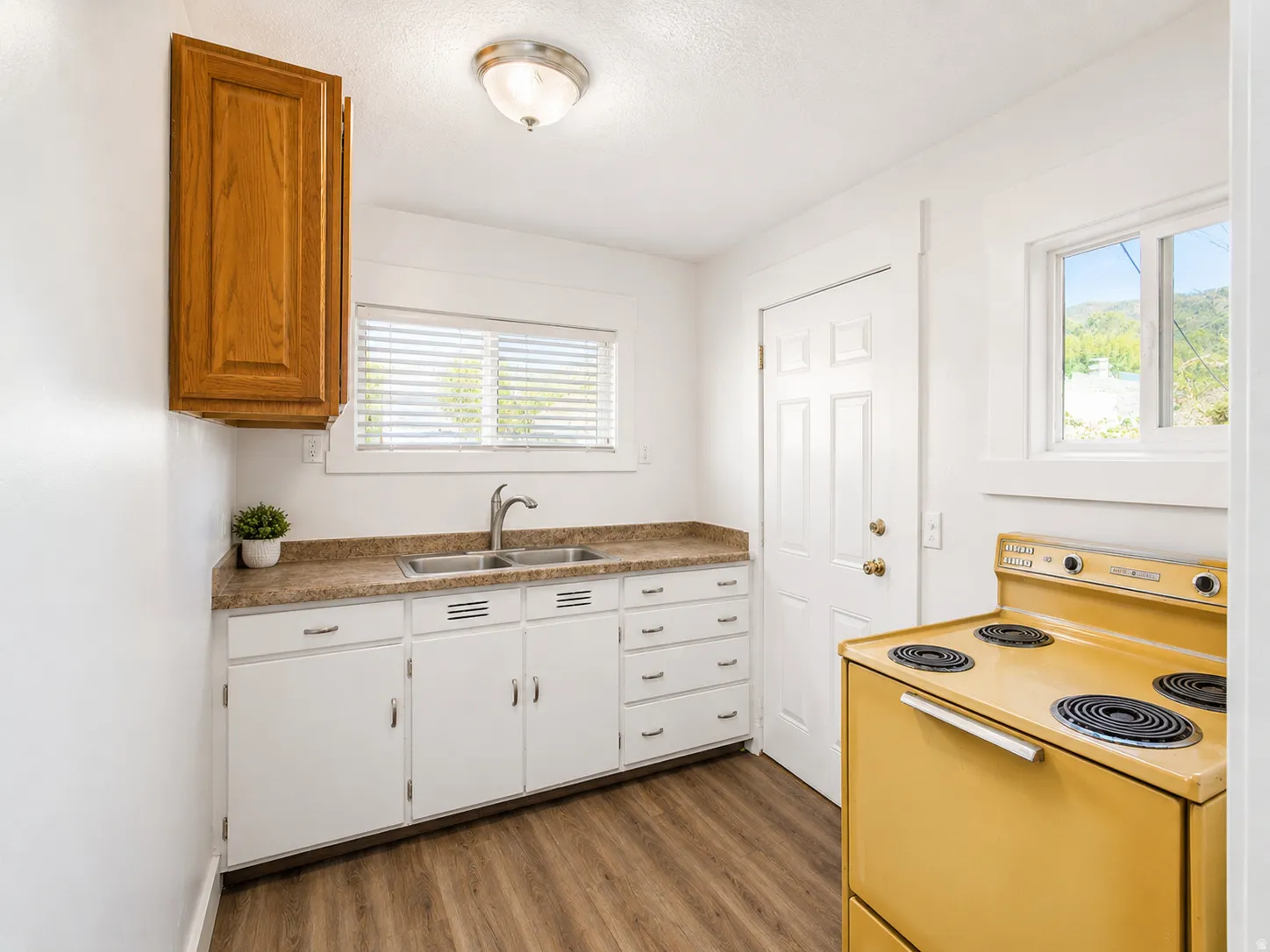 Kitchen featuring a double basin stainless steel sink, wood-finish flooring, white cabinetry, and a countertop with a textured finish