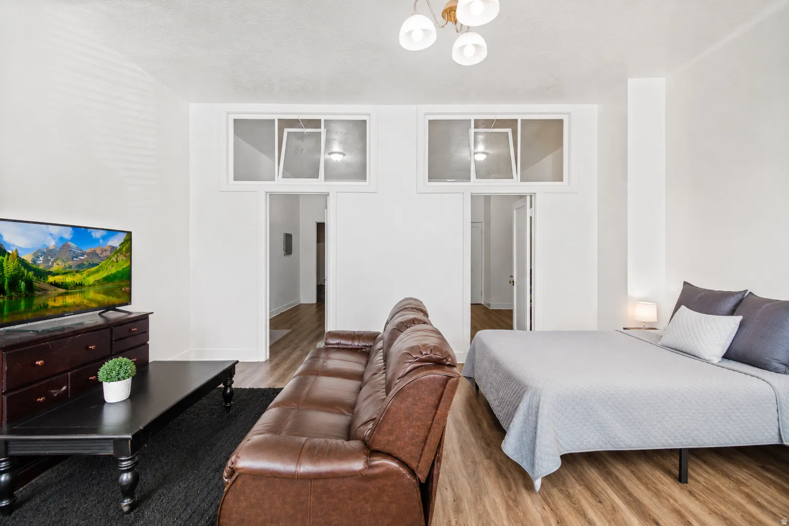 Open-concept living area with wood-finish flooring, white walls, and a contemporary ceiling light fixture