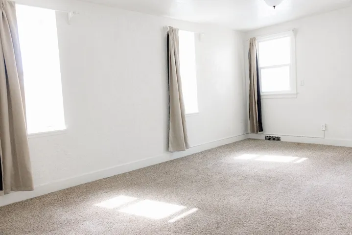 Spacious room featuring light-colored carpeting and white textured walls
