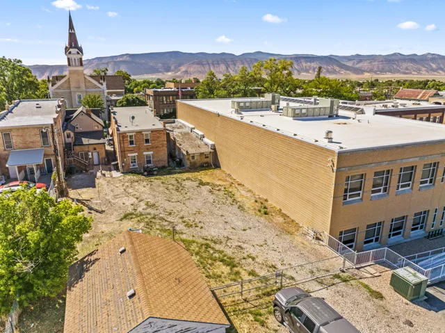 Expansive undeveloped lot with surrounding structures, featuring an adjacent brick building with multiple windows and a flat roof