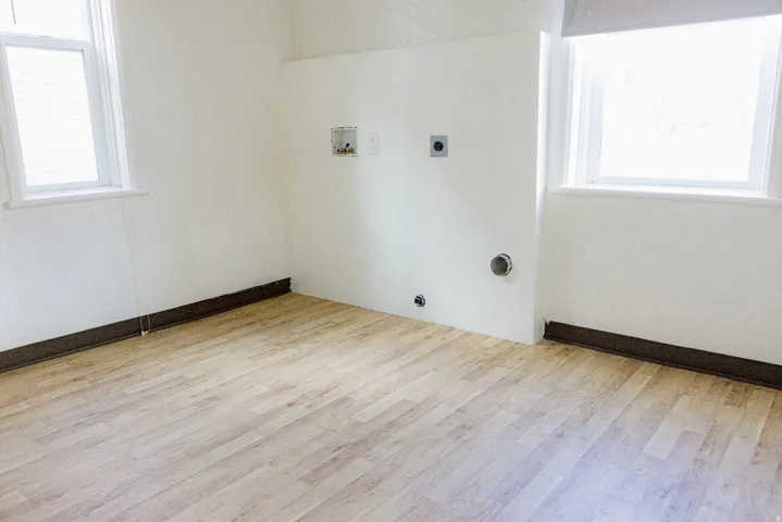 Dedicated utility space featuring light wood-finish flooring, two windows, and provision for laundry appliances