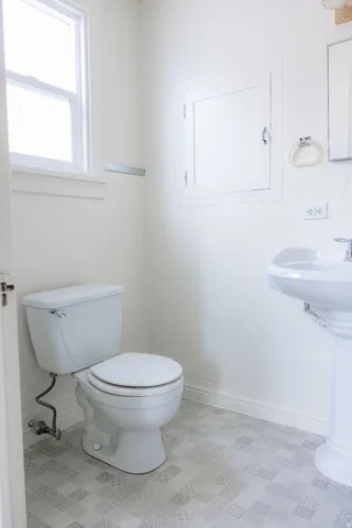 Bathroom with a pedestal sink, white toilet, and patterned tile-look flooring