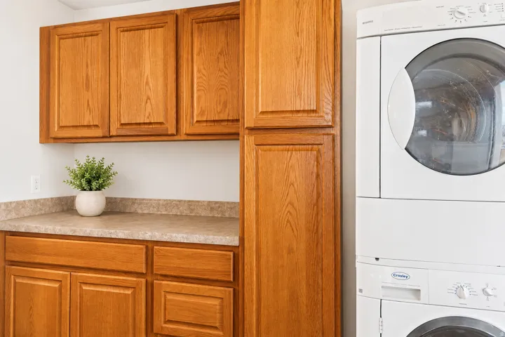 Laundry area featuring wood-finish cabinetry, a stacked washer and dryer, and a patterned countertop