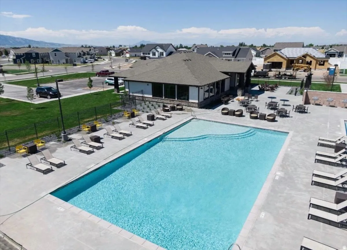 Expansive community pool area featuring a rectangular pool with integrated steps, a surrounding concrete deck, and an adjacent clubhouse with a stone facade