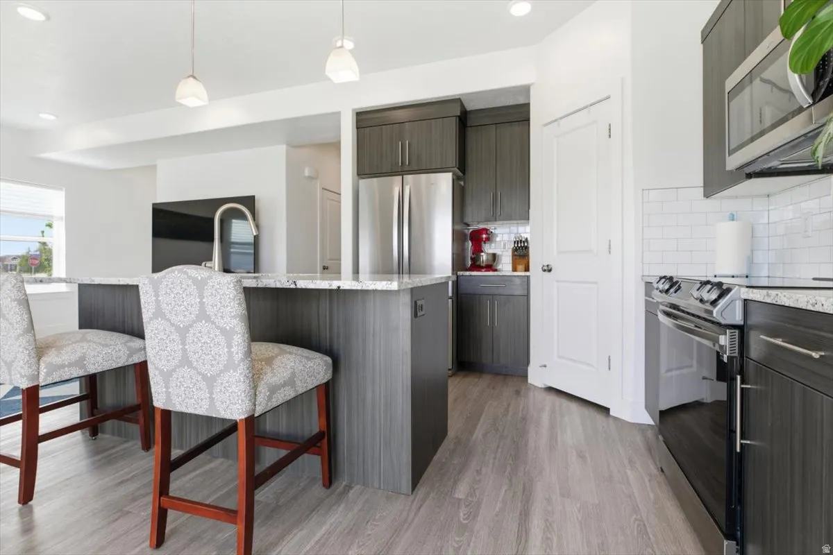 Open-concept kitchen featuring gray wood-finish cabinetry, stainless steel appliances, a kitchen island with seating, pendant lighting, and wood-finish flooring