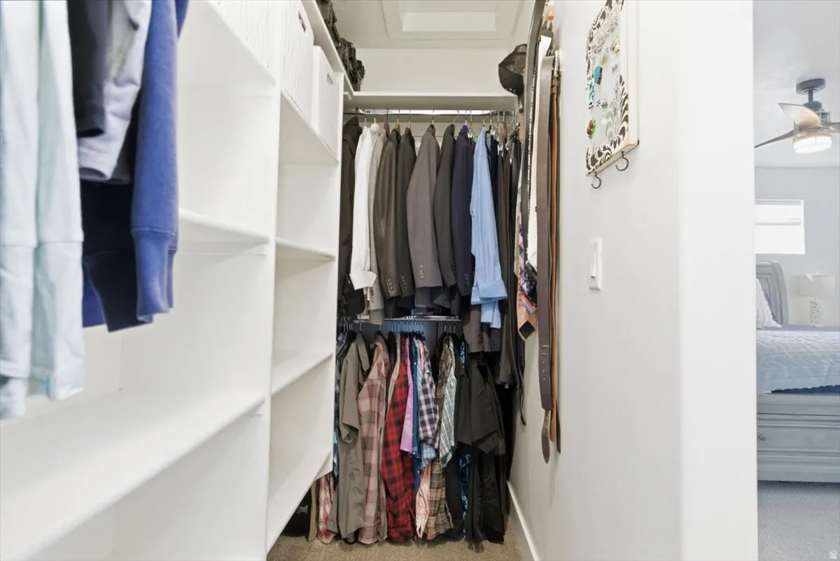 Walk-in closet with white shelving units, multiple clothing rods, and light-colored walls