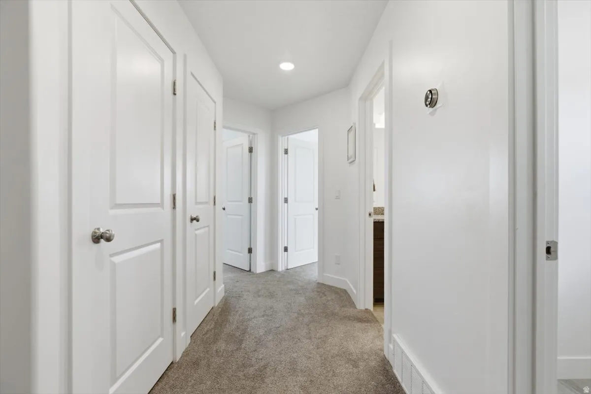 Hallway featuring light gray carpet flooring, recessed lighting, white paneled doors with brushed nickel hardware, and white baseboards