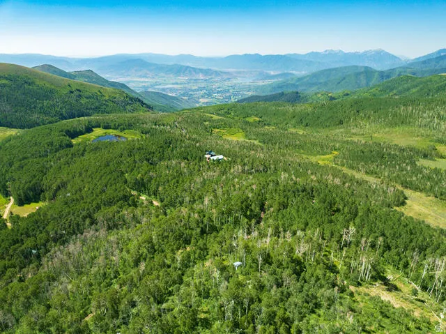 Expansive mountainous terrain featuring dense forests, a natural pond, and distant valley scenery
