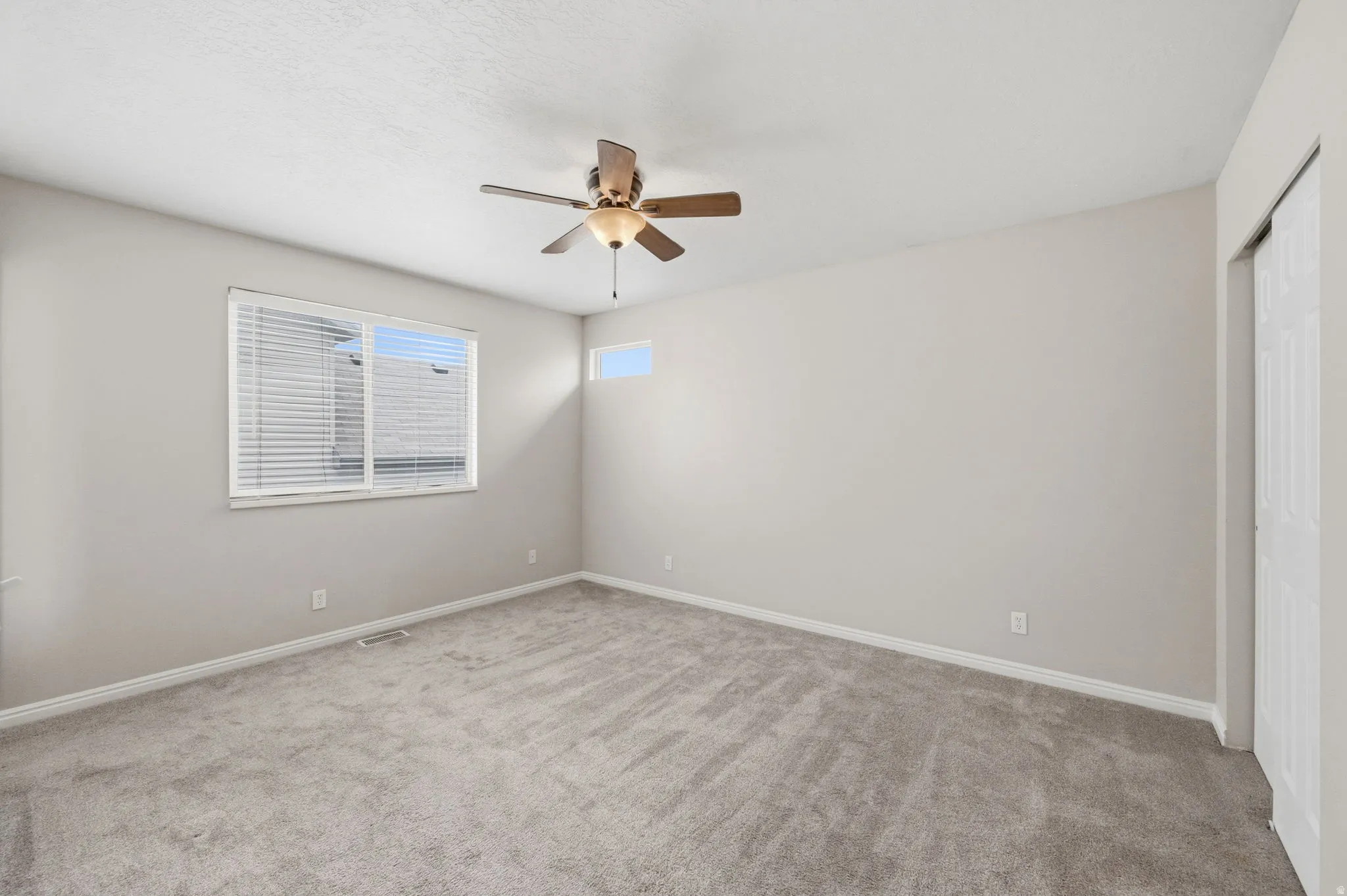 Carpeted room featuring a ceiling fan with integrated lighting, a large horizontal window with blinds, a high transom window, and white bi-fold closet doors