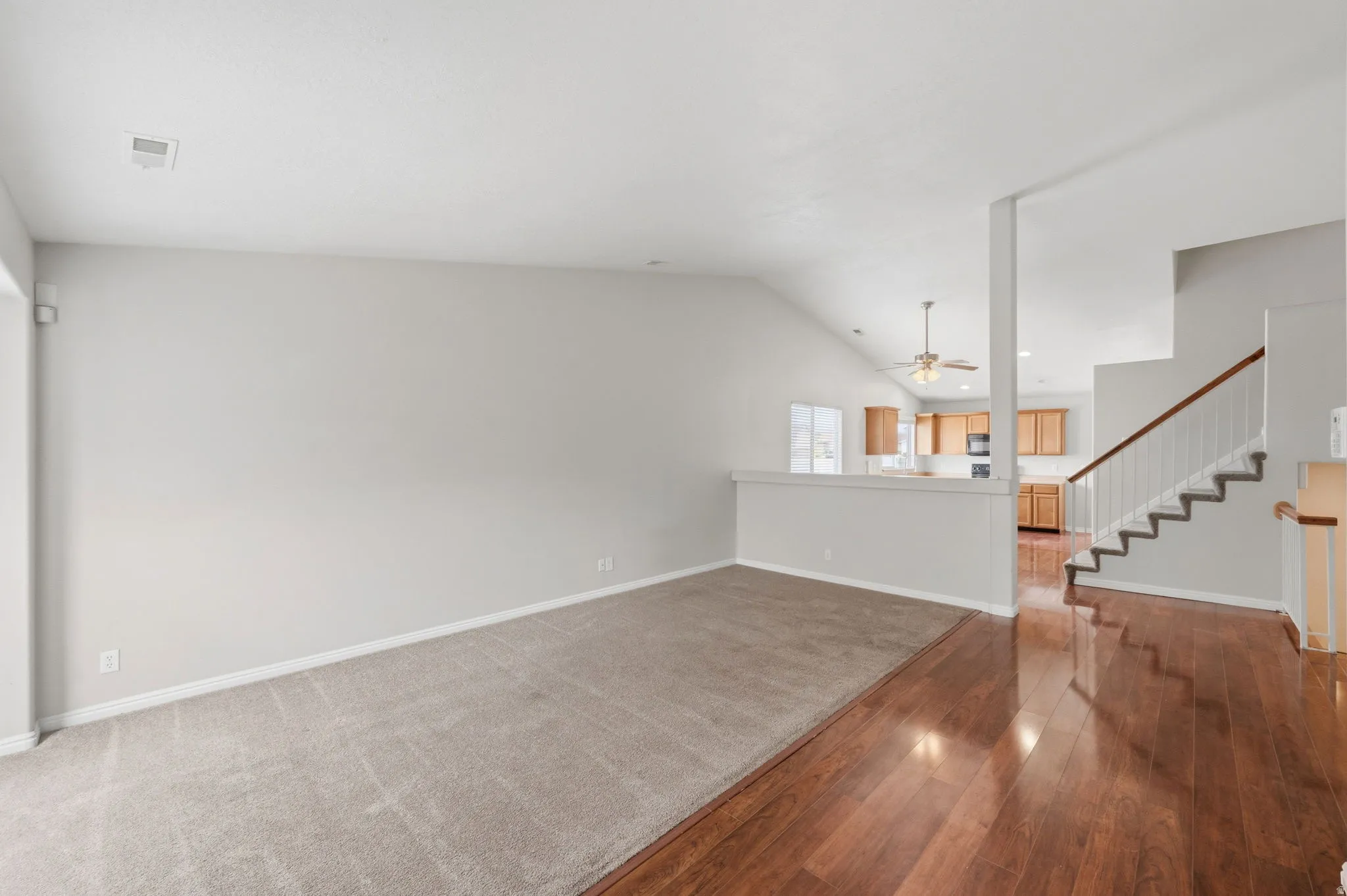 Spacious room featuring vaulted ceilings, light gray wall paint, and a combination of wood-finish flooring and carpeting