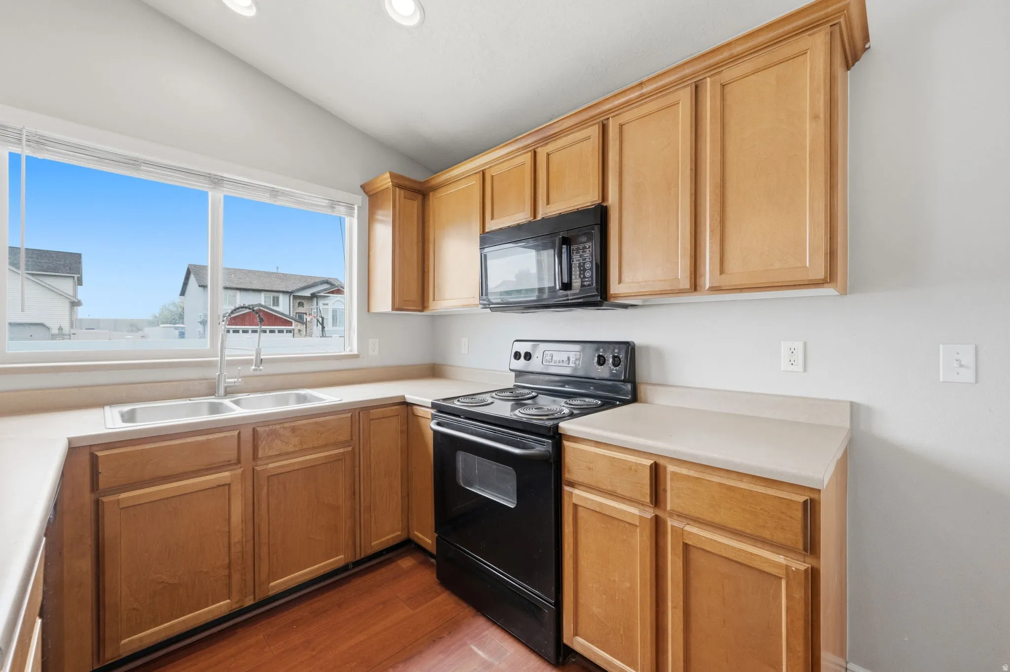Kitchen featuring wood-finish cabinetry, light-toned countertops, a stainless steel double basin sink, and wood-finish flooring