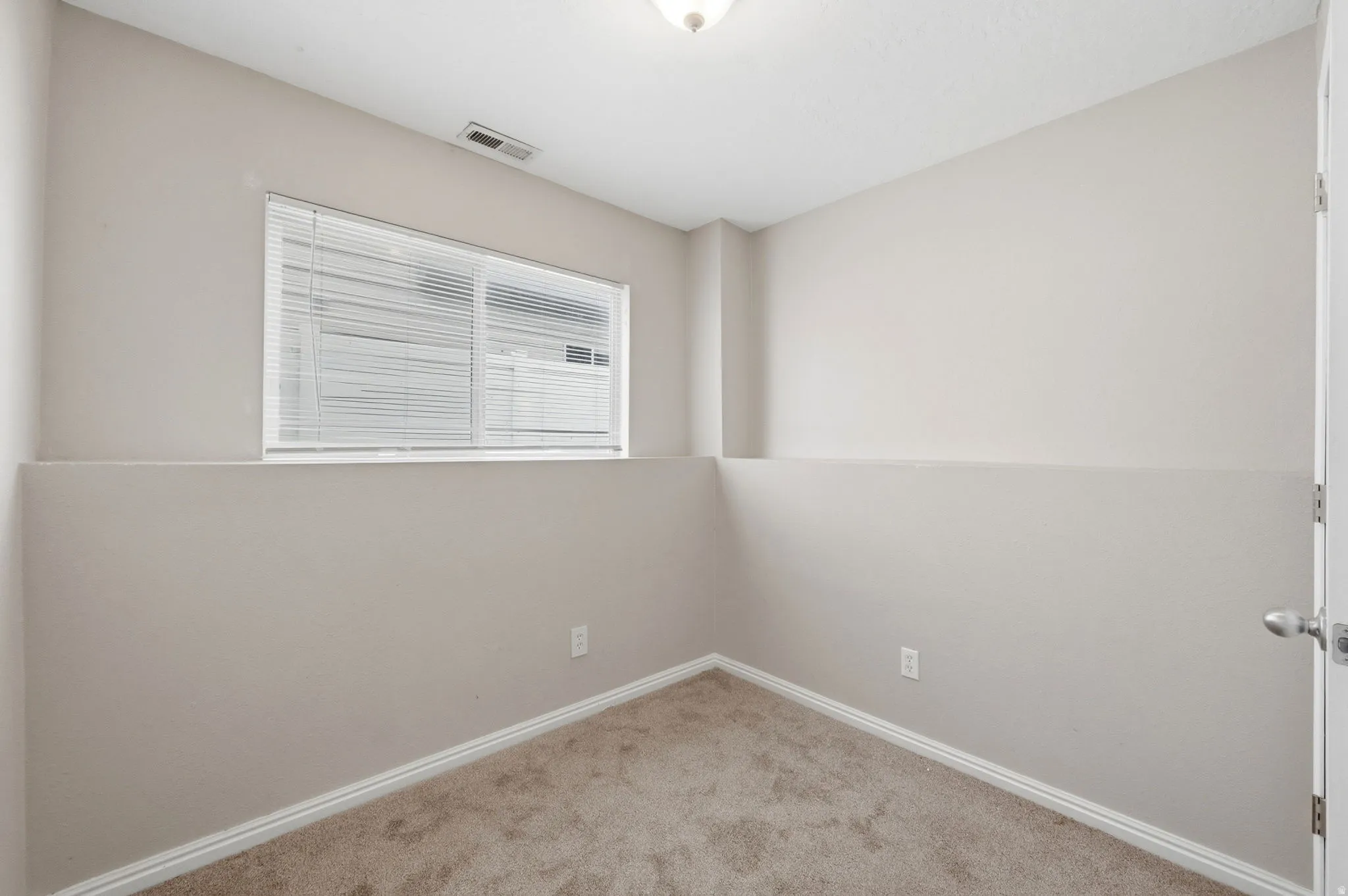Neutral-toned room featuring a window with white blinds, light beige carpeting, and white baseboards