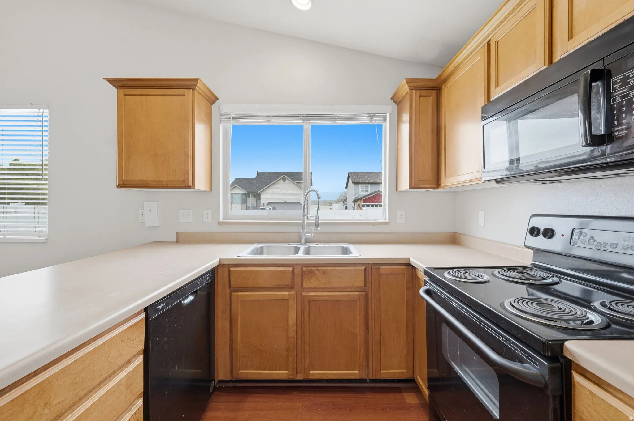 Kitchen featuring wood-finish cabinetry, light-toned countertops, a stainless steel double basin sink with a chrome faucet, and integrated black appliances including a range and microwave