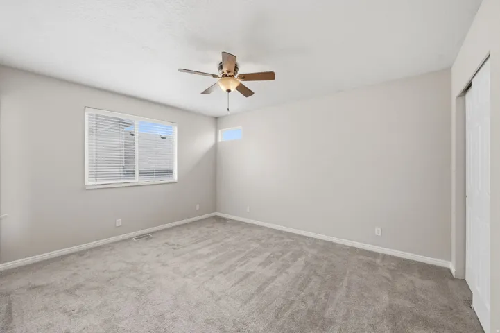 Carpeted room featuring a ceiling fan with integrated lighting, a large horizontal window with blinds, a high transom window, and white bi-fold closet doors