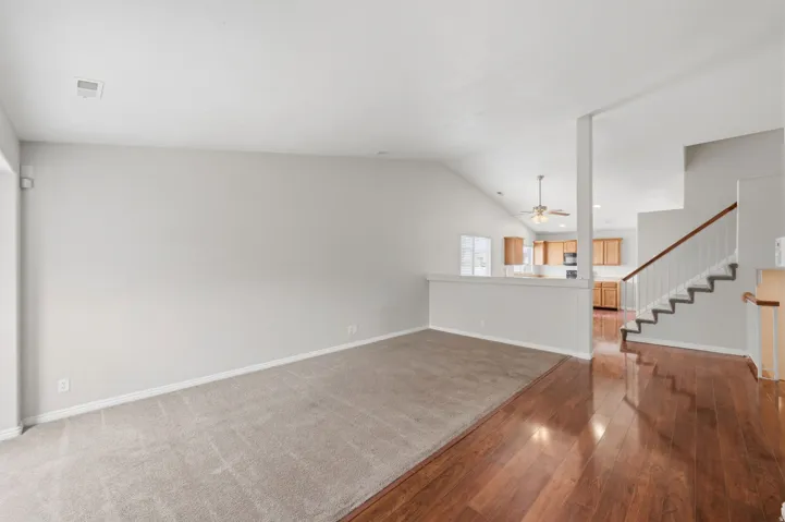 Spacious room featuring vaulted ceilings, light gray wall paint, and a combination of wood-finish flooring and carpeting