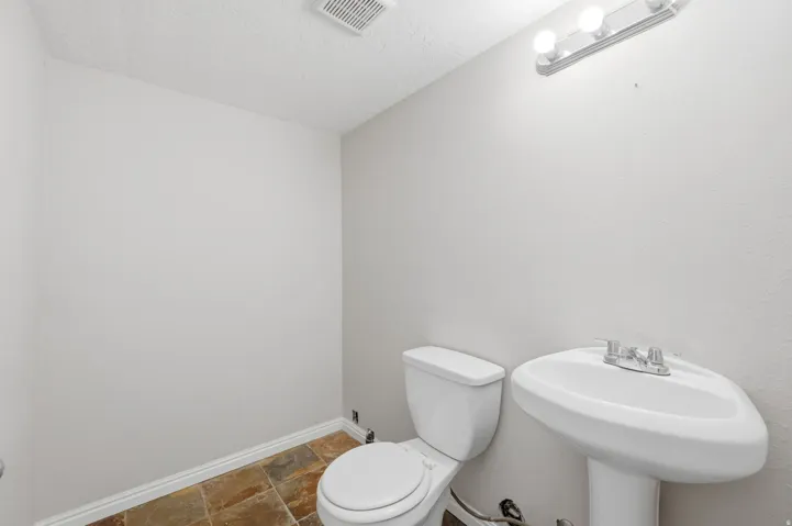 Bathroom featuring neutral wall paint, a white pedestal sink, a white two-piece toilet, and multi-toned tile flooring