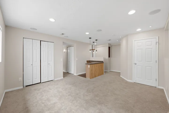 Spacious room featuring neutral carpet, recessed lighting, a built-in bar with pendant lights, and multiple bi-fold closet doors