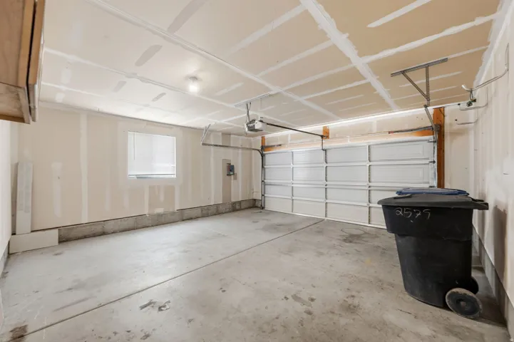Spacious two-car garage with a concrete floor, an overhead garage door, built-in overhead lighting, a single window with blinds, and exposed ceiling joists