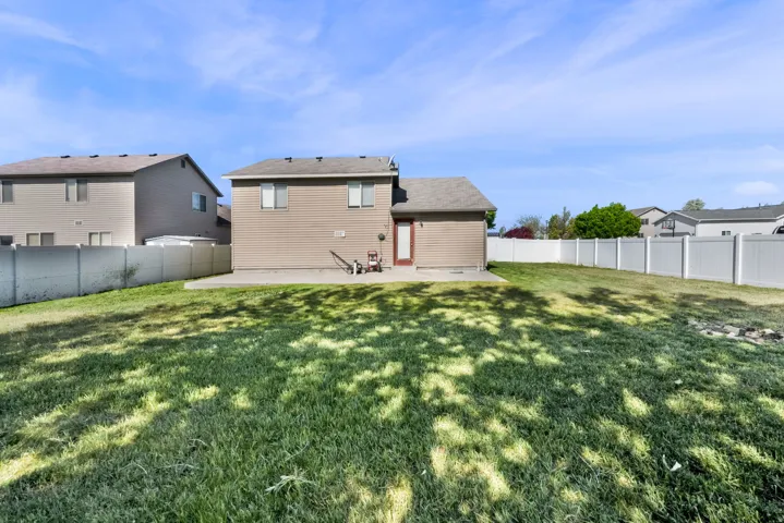 Expansive backyard featuring a large green lawn, concrete patio, and full perimeter white vinyl fencing