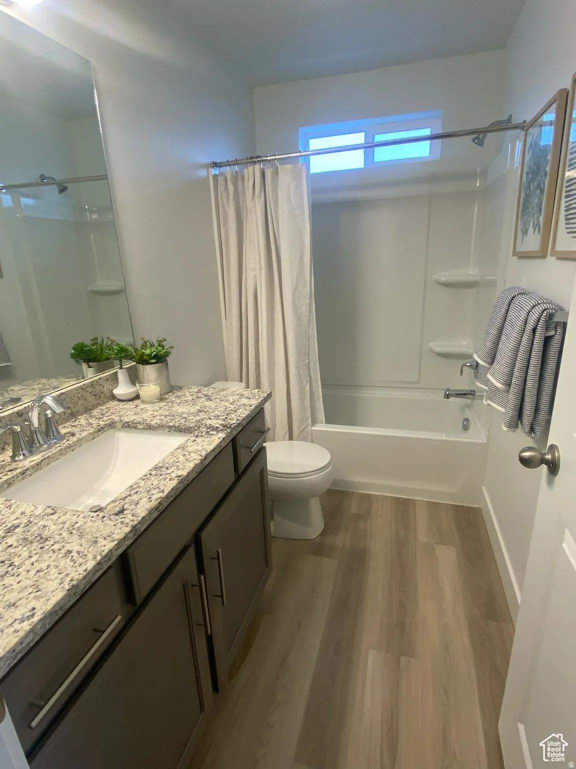 Bathroom featuring a modern vanity with a rectangular sink and granite-finish countertop, wood-finish flooring, a full-size bathtub with shower, and a high-set window