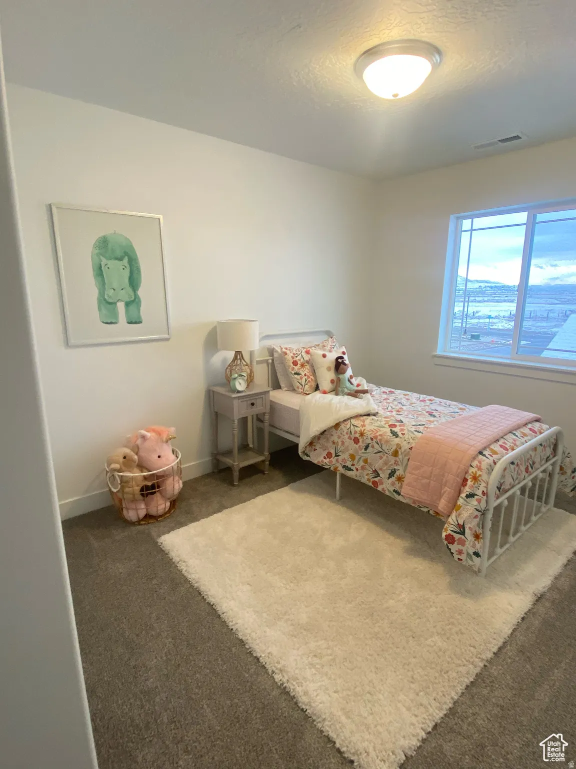 Room featuring neutral wall paint, carpet flooring, a window with horizontal muntins, a flush mount ceiling light fixture, and a single-tier nightstand