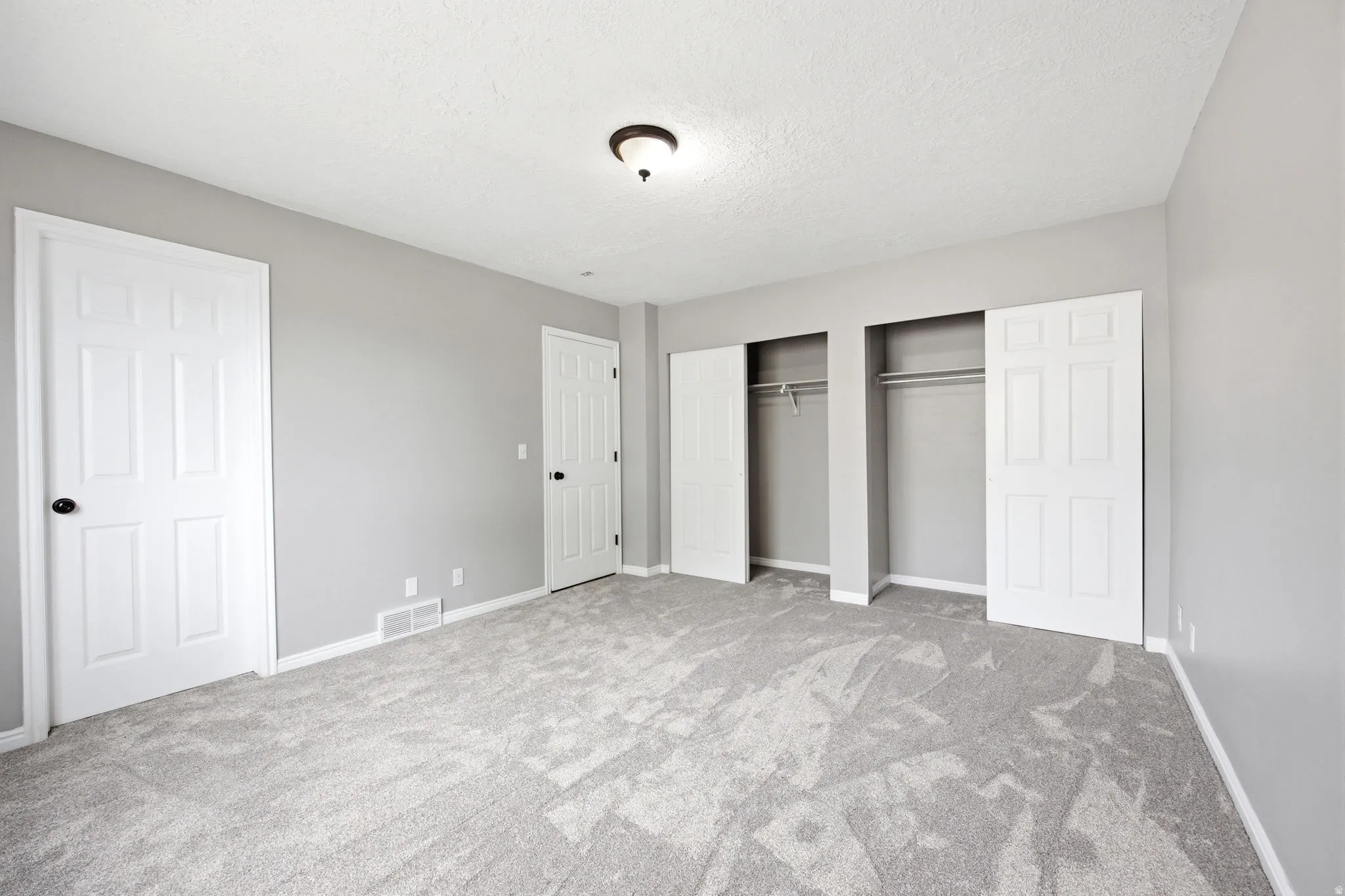 Spacious room featuring light gray walls, new gray patterned carpet, and bright white trim