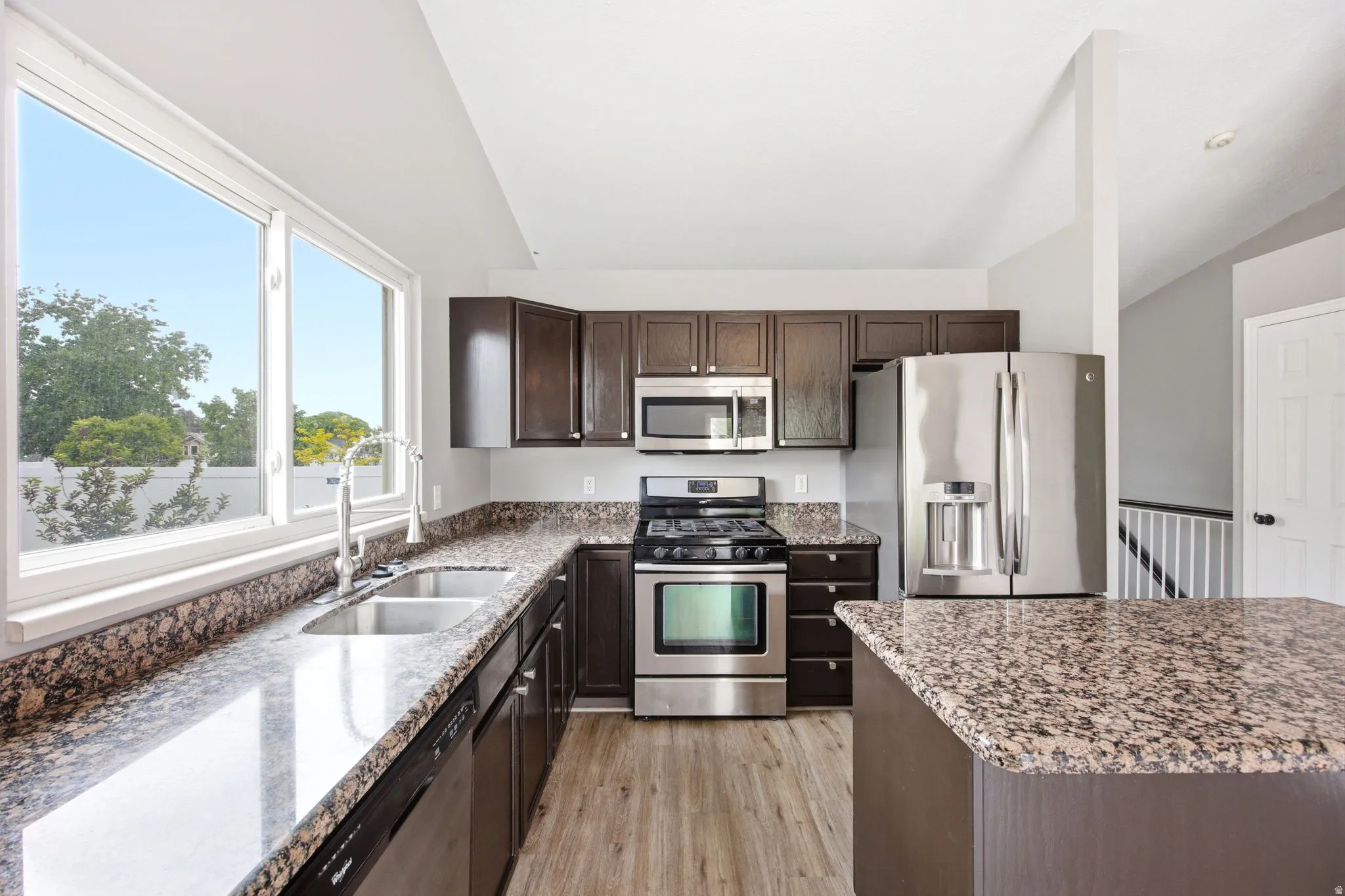 Kitchen featuring dark wood cabinetry, stainless steel appliances, a double basin sink, and wood-finish flooring