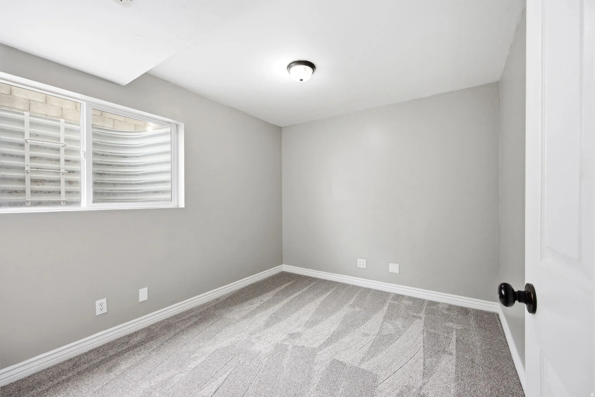 Soft gray wall finish, plush patterned carpeting, white trim, and a window with a security grate