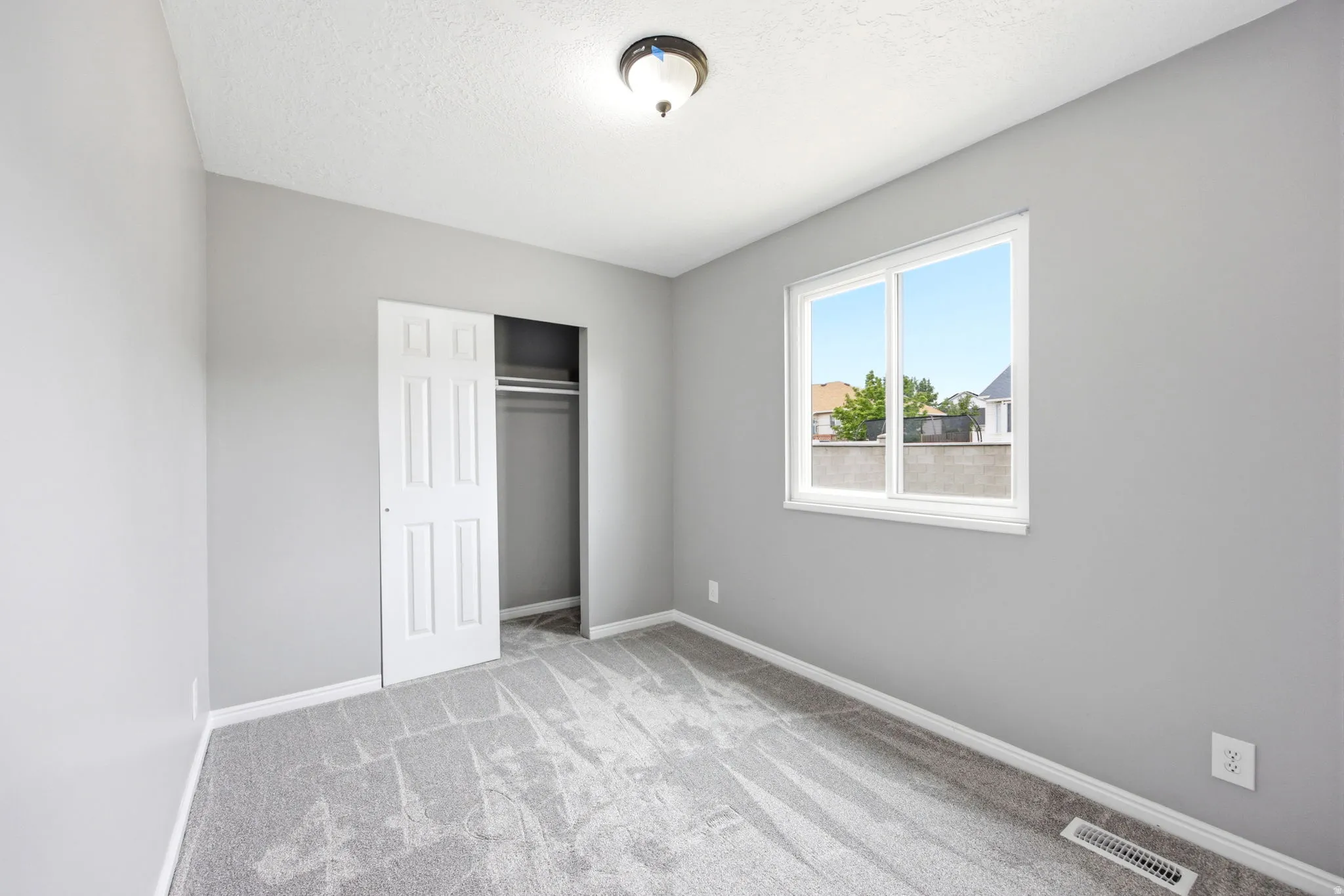 Carpeted room with a double-pane window, featuring a sliding closet door with a built-in hanging rod, a ceiling-mounted light fixture, and light gray walls