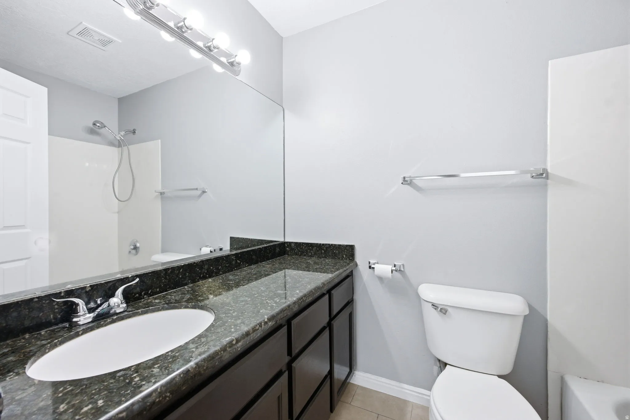 Bathroom vanity featuring a dark granite countertop with an oval undermount sink and chrome faucet