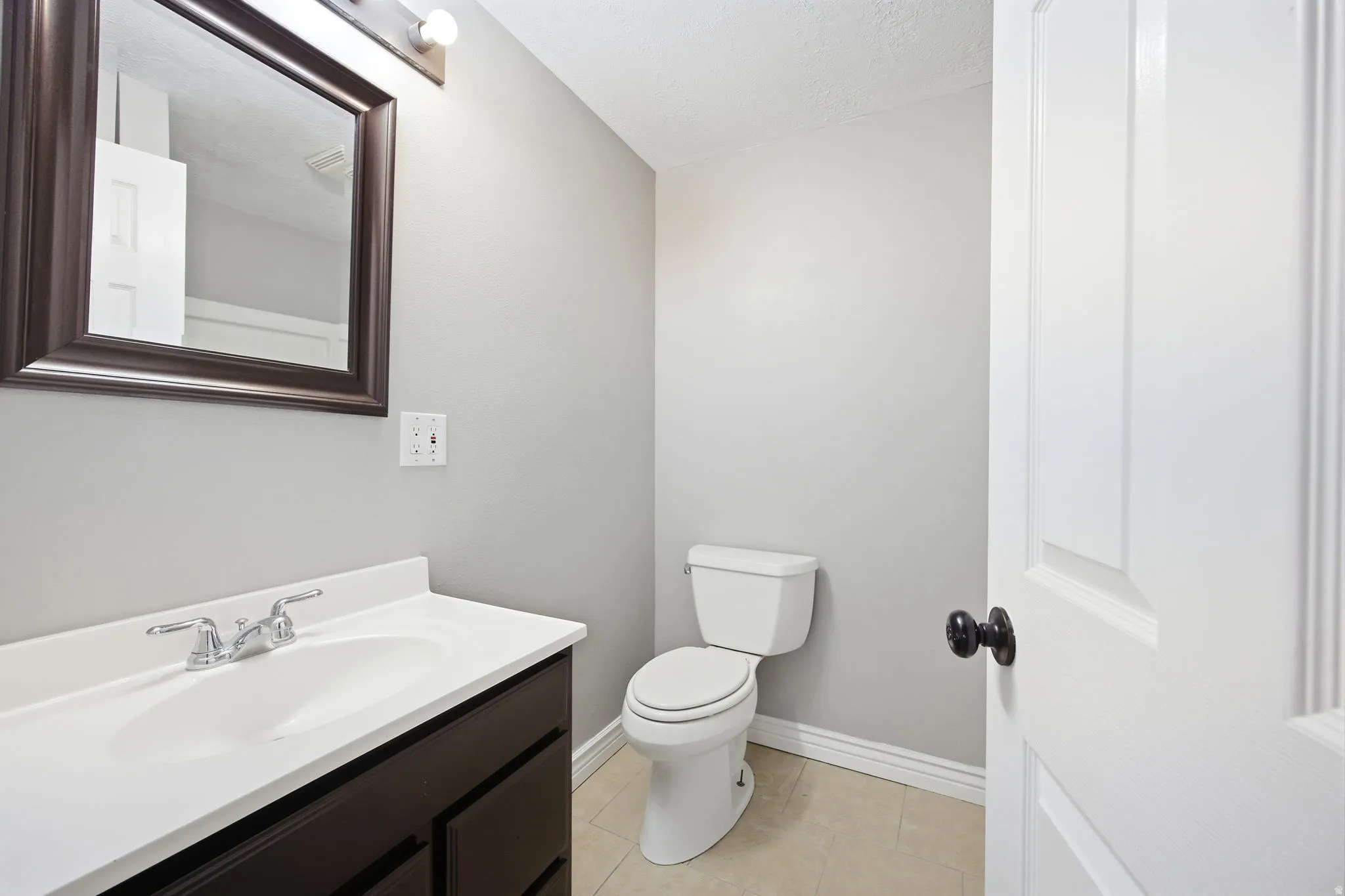 Bathroom featuring a dark wood-finish vanity with an integrated white sink, chrome faucet, and rectangular framed mirror