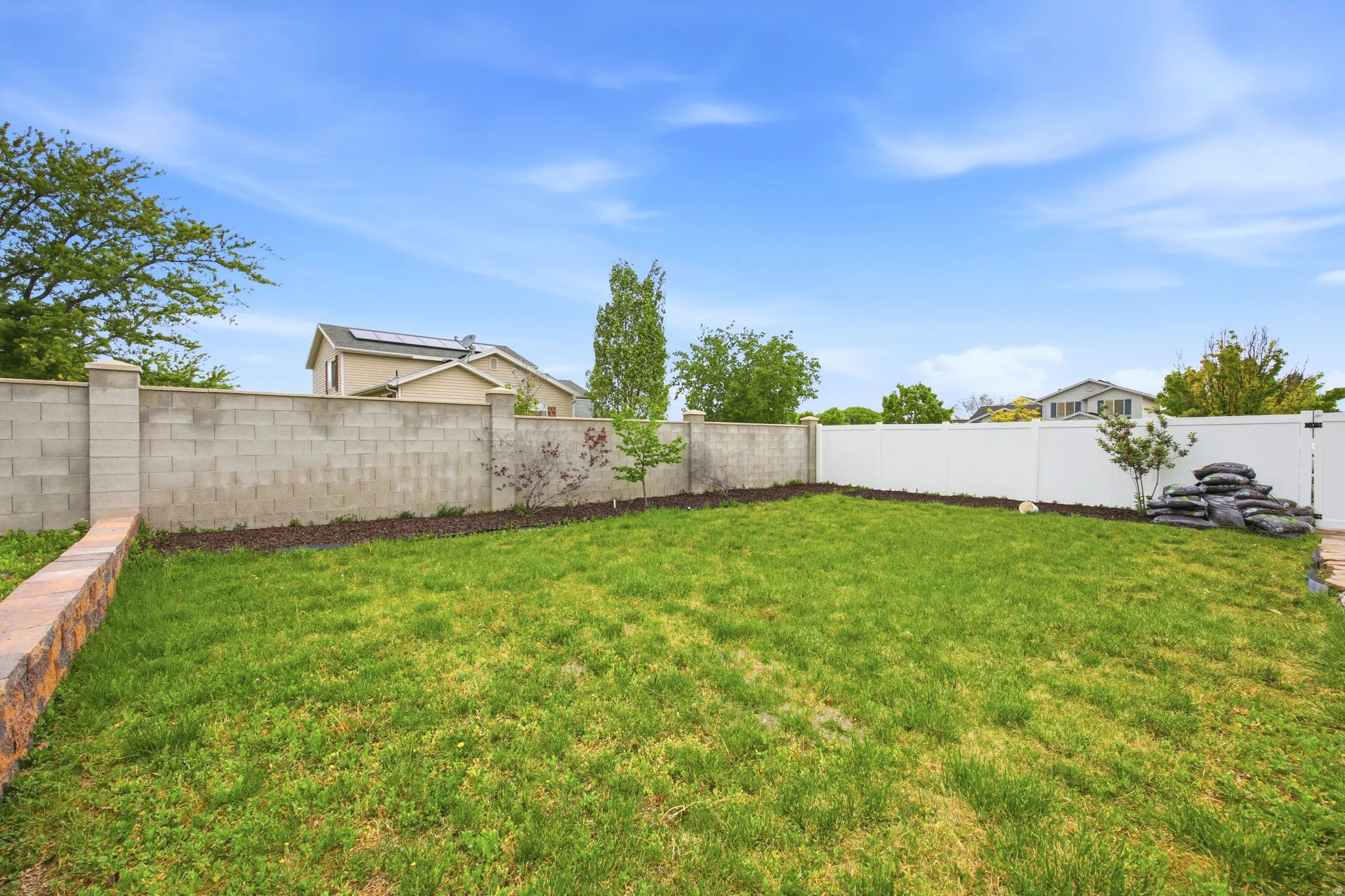 Expansive grassy yard with a block wall perimeter and a white privacy fence