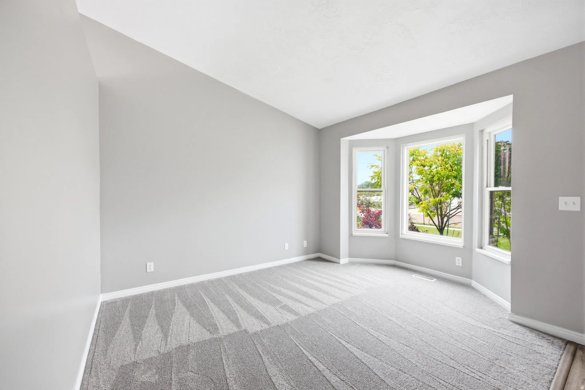 Room with a bay window, light gray walls, white trim, and patterned gray carpet