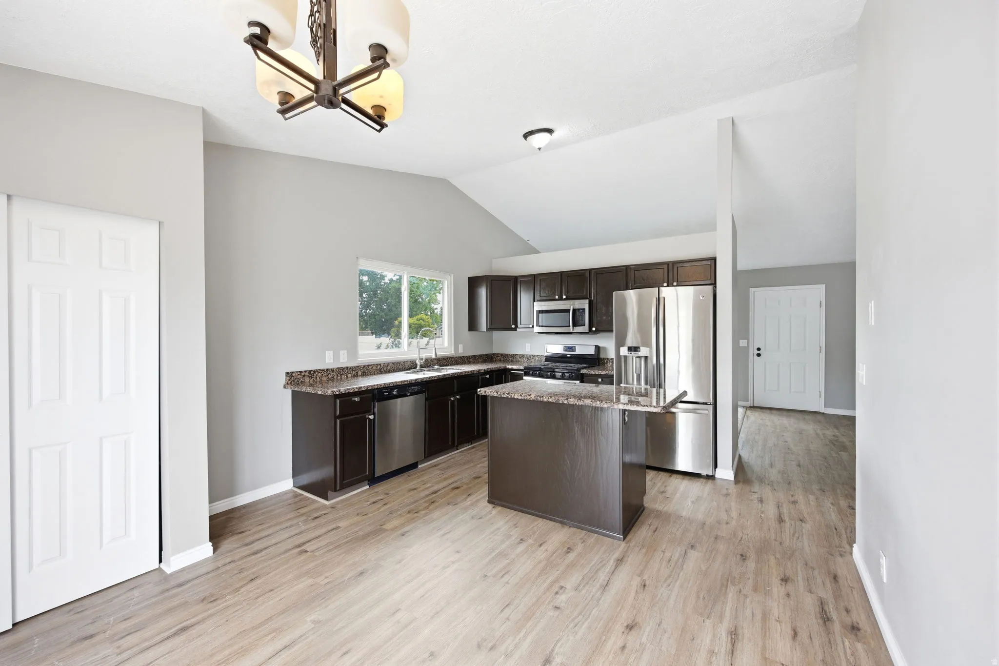 Open-concept kitchen and dining area featuring vaulted ceilings and wood-finish flooring