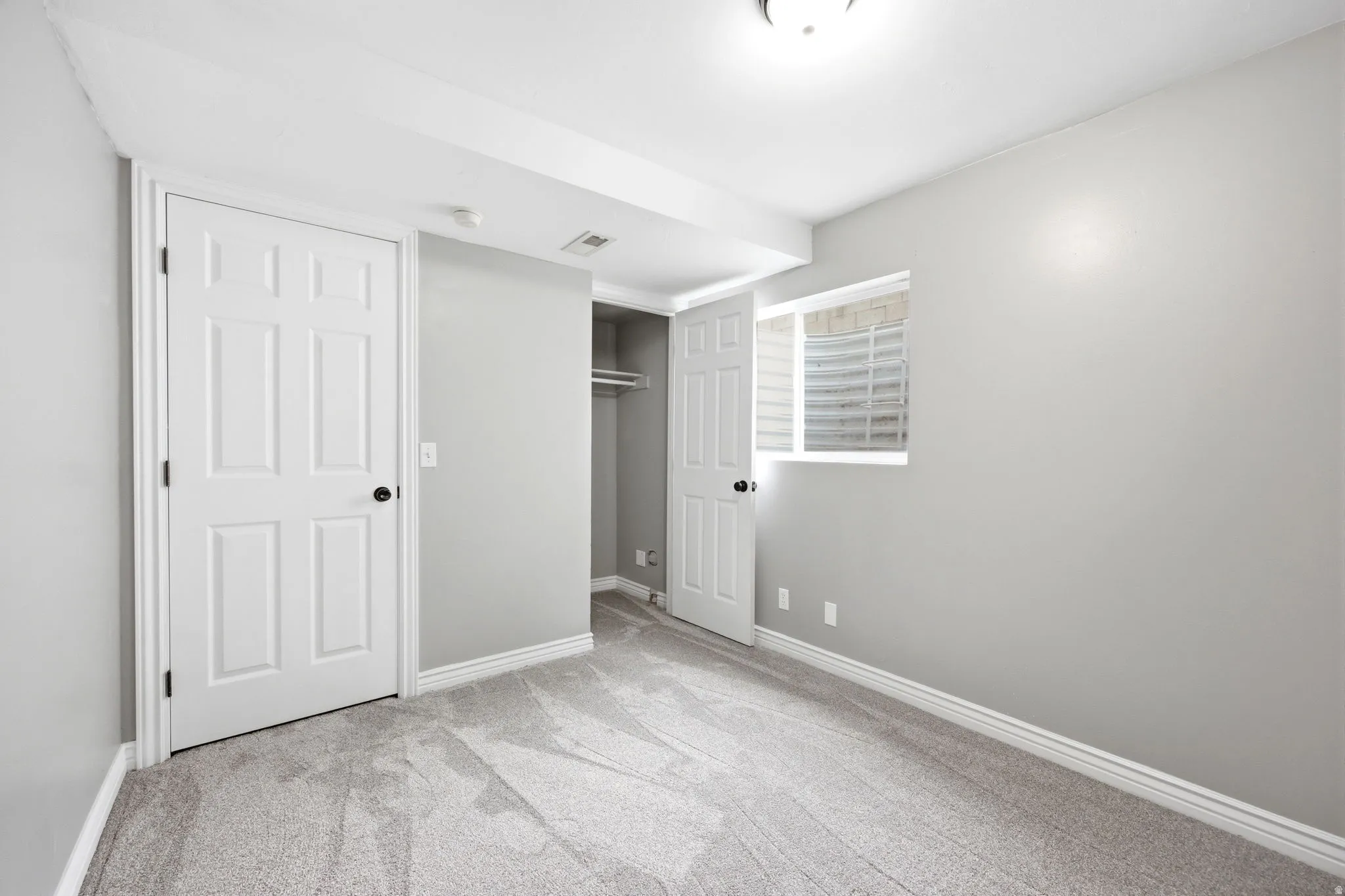 Room featuring light gray wall paint, white trim, gray patterned carpet, a built-in closet with hanging rod, and a window with horizontal blinds
