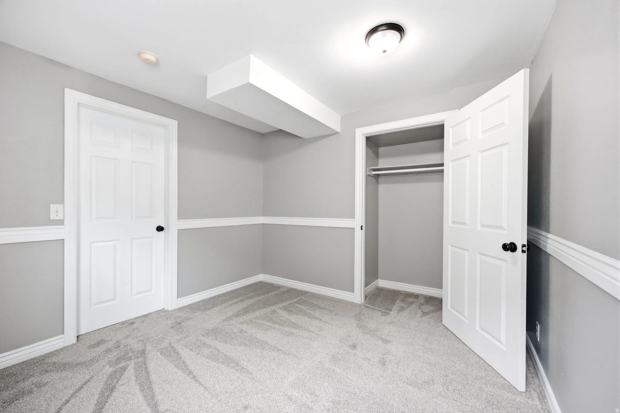 Carpeted room with light gray walls, white trim, and a white six-panel door