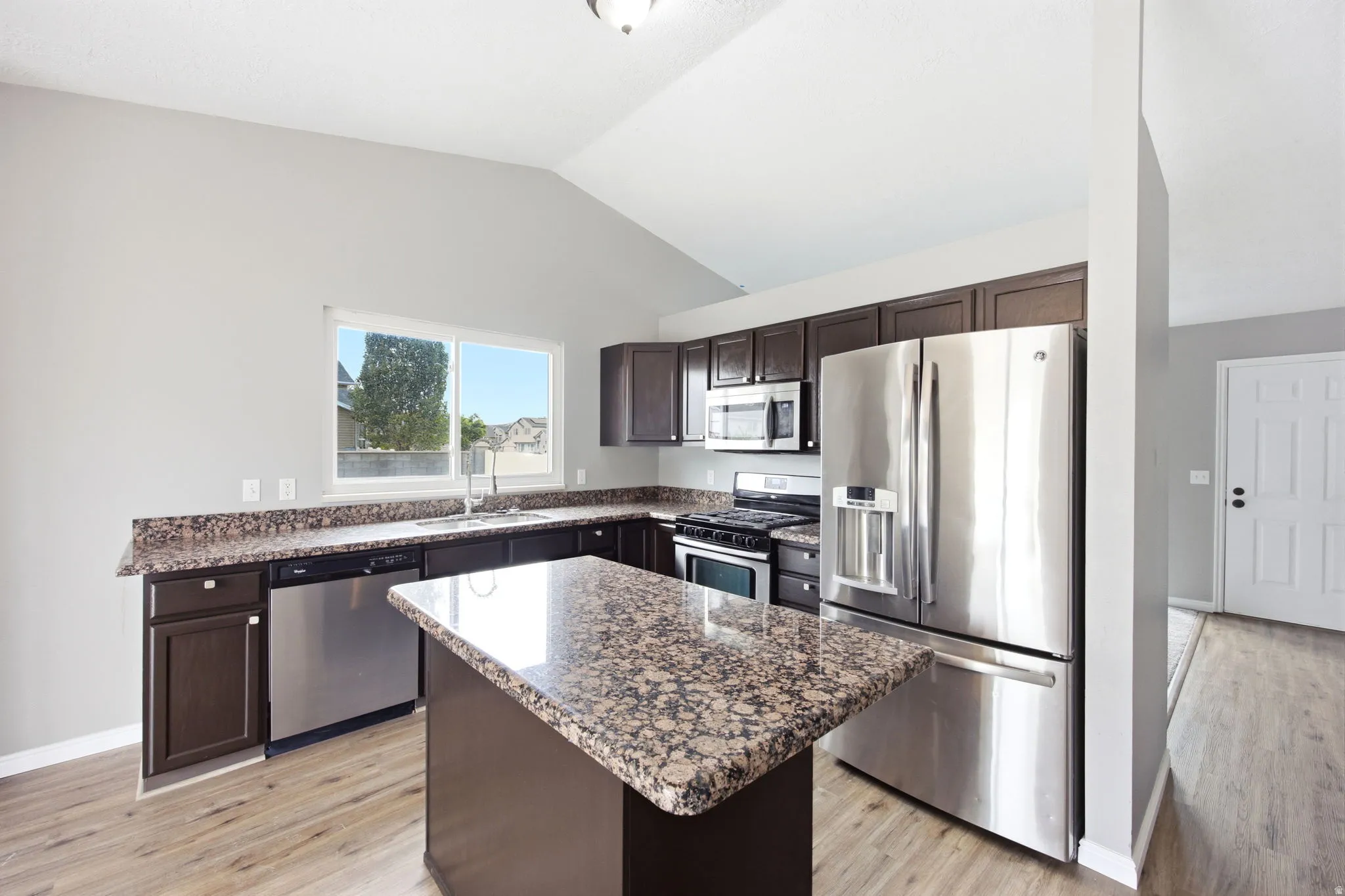 Kitchen featuring a central island, dark wood-finish cabinetry, stainless steel appliances, granite countertops, and wood-finish flooring