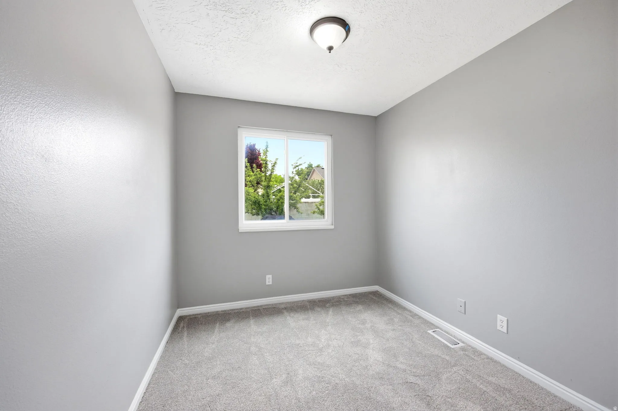 Room featuring light gray textured walls, gray carpeted flooring, and white baseboards