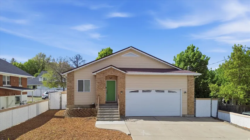 Exterior featuring beige siding, brick accents, an attached garage with a white door, a bright green front door, and a concrete driveway