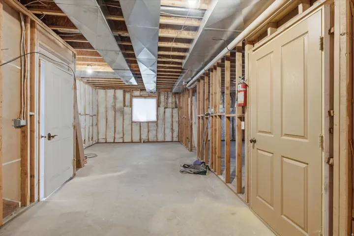 Unfinished basement featuring exposed wood framing, concrete flooring, ductwork, and a window for natural light