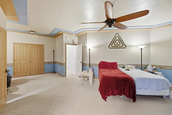 Spacious room featuring neutral carpeting, a tray ceiling with accent molding, a ceiling fan, and double bi-fold doors