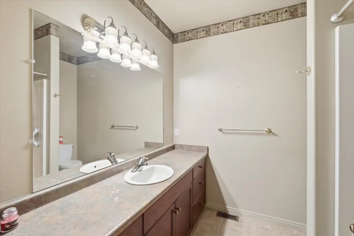 Bathroom featuring an extended vanity with dual integrated sinks, an expansive wall-mounted mirror, and an overhead multi-bulb light fixture