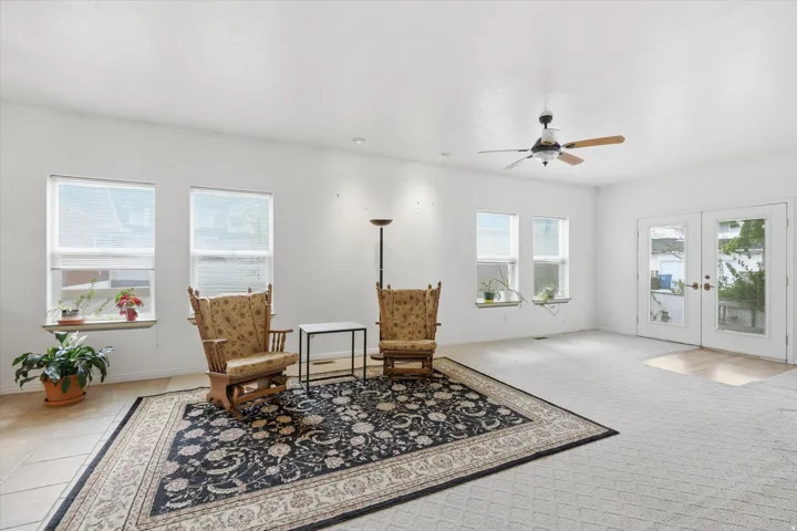 Spacious room featuring multiple windows, white walls, a ceiling fan with integrated lighting, and French doors providing external access