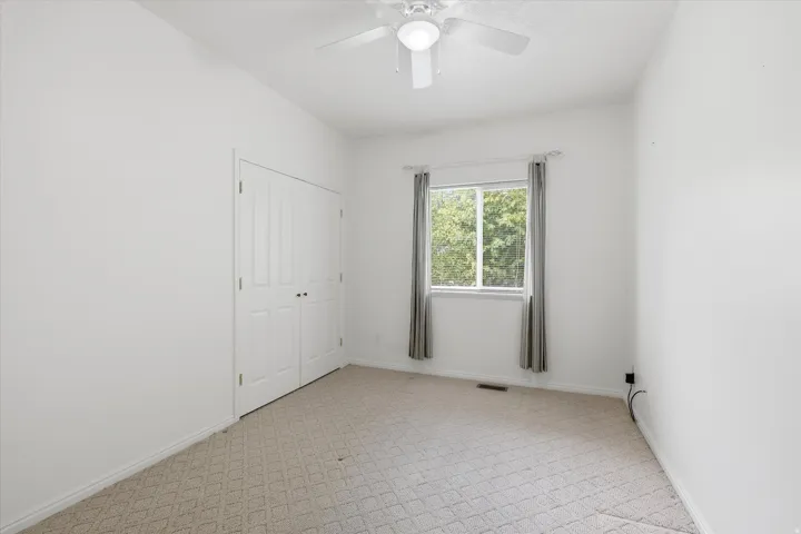 White-painted room featuring light-colored patterned carpet, a ceiling fan with light, and a double-door closet