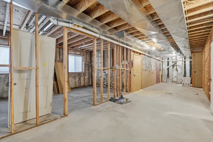 Unfinished basement with concrete flooring, exposed wood framing, and visible ductwork