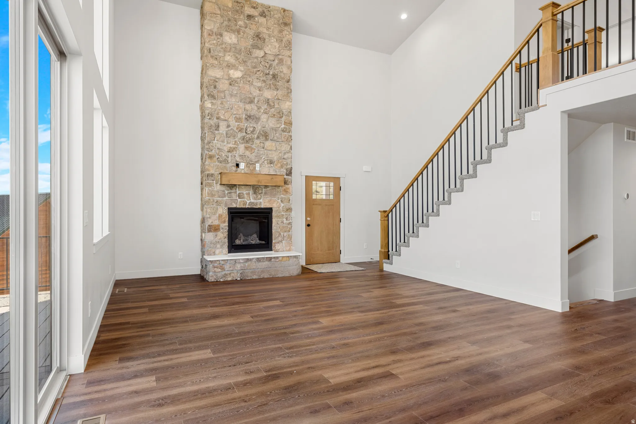 Spacious living area featuring a floor-to-ceiling stone fireplace with a wood mantel, rich wood-finish flooring, and expansive windows